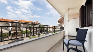 Un balcón con una silla, barandilla y vistas a edificios con tejados rojos.