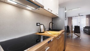 Una cocina moderna con placa de inducción, hervidor y cafetera. Cuenta con encimera de madera y mesa de comedor de vidrio con sillas.