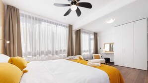 Una habitación de hotel con una cama grande, un ventilador de techo, un escritorio con una silla, un espejo y un armario.
