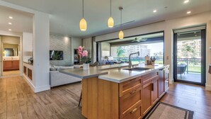 A modern kitchen with a large island, pendant lights, and a view of a residential area.