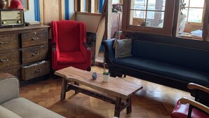 A room with a wooden floor, a red armchair, a blue sofa, a wooden coffee table, and a vintage radio. - Awesome View, Valparaiso Terrace (Valparaíso)