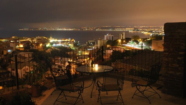 A terrace with a round table and chairs, overlooking a cityscape with a body of water and distant city lights. - Awesome View, Valparaiso Terrace (Valparaíso)