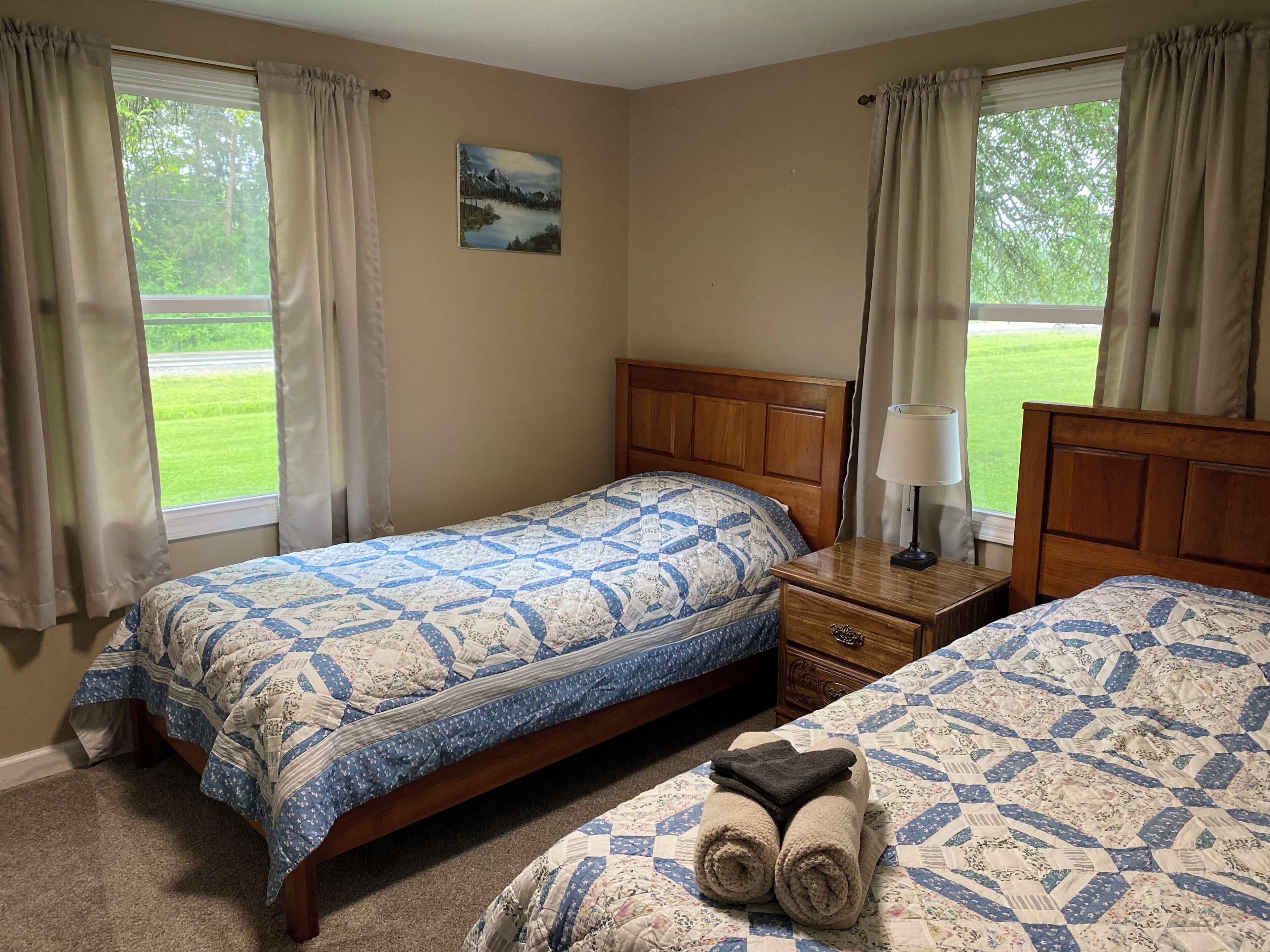 A bedroom with two beds, a wooden headboard, a nightstand with a lamp, and a painting on the wall.