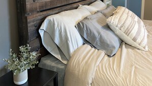 Una camera da letto con una testiera in legno, un comodino con una pianta e un letto con numerosi cuscini e una coperta.