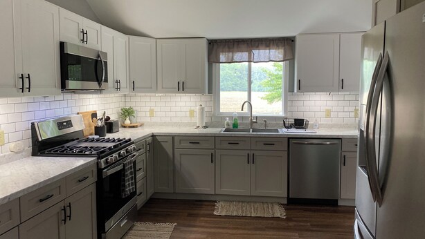 Una cucina moderna con mobili bianchi, elettrodomestici in acciaio inossidabile e una finestra che fa entrare luce naturale.