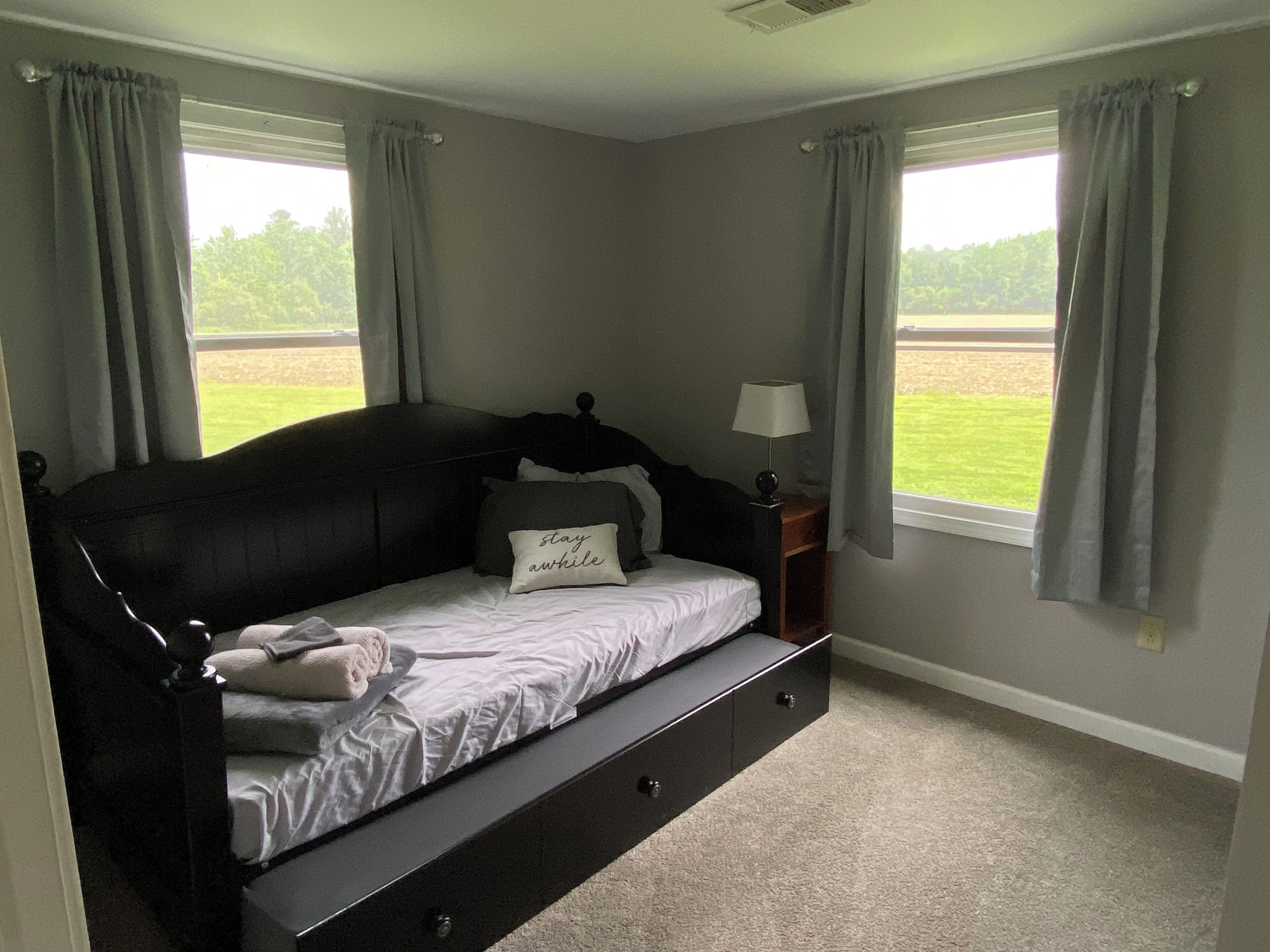 A bedroom with a bed, a nightstand, a lamp, and two windows with curtains.