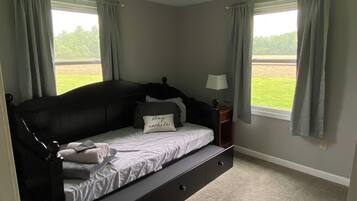 A bedroom with a bed, a nightstand, a lamp, and two windows with curtains.