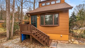 Una baita di legno con una scala che conduce a un patio, circondata da alberi.