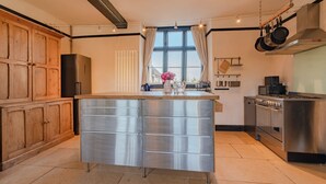 Een moderne keuken met een centraal eiland, roestvrijstalen apparatuur, houten keukenkastjes en een groot raam met gordijnen.