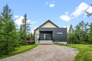 A modern two-story building with a dark exterior, a wooden deck, and a gravel driveway.