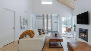 A modern living room with a high ceiling, a fireplace, and a large window. - Hôtel à la maison - Villa Skáli (Shannon)