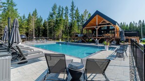 A pool area with lounge chairs and umbrellas, surrounded by tall trees and a lodge with a wooden exterior. - Hôtel à la maison - Villa Skáli (Shannon)