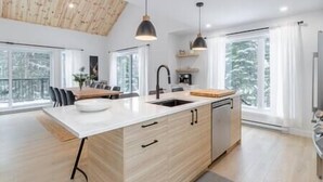 A modern kitchen with a large island, pendant lighting, and a view of snowy trees through large windows. - Hôtel à la maison - Villa Skáli (Shannon)