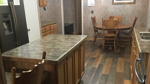 A kitchen with wooden cabinets, a granite countertop, a dining table with chairs, and a refrigerator. - Centrally located between Bryson City, Sylva and Cherokee.5 mins to the Casino. (Whittier)