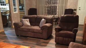 A living room with a brown leather sofa, a wooden coffee table, and a brown leather armchair. There is a patterned curtain and a white door in the background. - Centrally located between Bryson City, Sylva and Cherokee.5 mins to the Casino. (Whittier)
