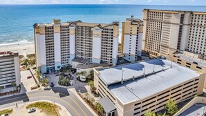 Un hotel de gran altura con varios pisos, un estacionamiento y vista a la playa y al océano.