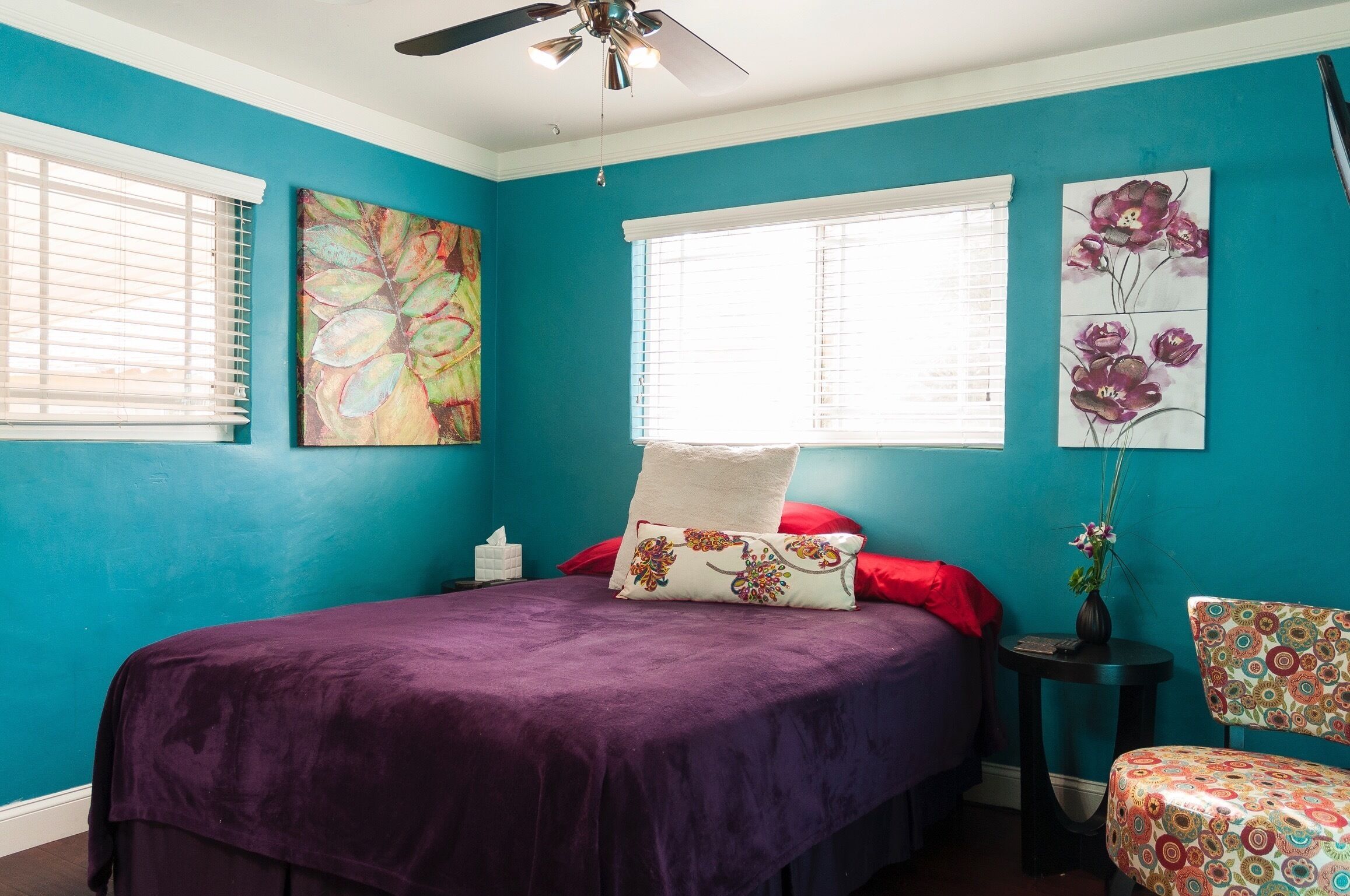 A bedroom with teal walls, a purple bedspread, and two paintings.