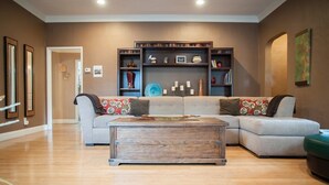 Un salon comprenant un canapé d’angle, une table basse en bois et des étagères intégrées ornées d’objets décoratifs.
