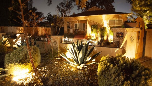 Une maison dotée d’un patio couvert, d’un petit jardin avec différentes plantes et d’une entrée bien éclairée.
