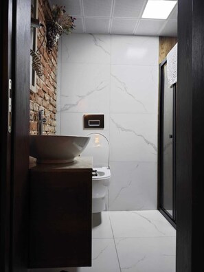 Un baño moderno con piso de mármol, tocador de madera, inodoro blanco y cabina de ducha de vidrio.