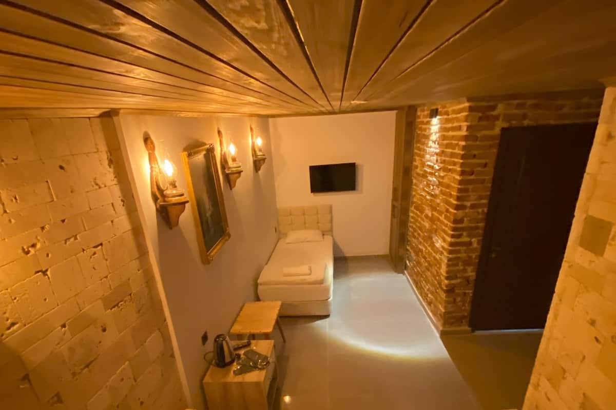 A narrow, dimly lit room with two beds, a small table, and a wall-mounted TV.