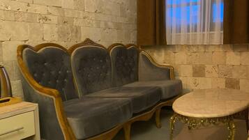 A room with a grey upholstered sofa, a small round table, and a white nightstand.
