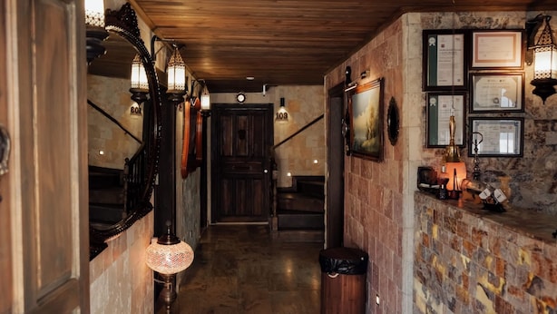 A narrow hallway with wooden flooring, a staircase, and a wall adorned with framed certificates and a small table with decorative items.
