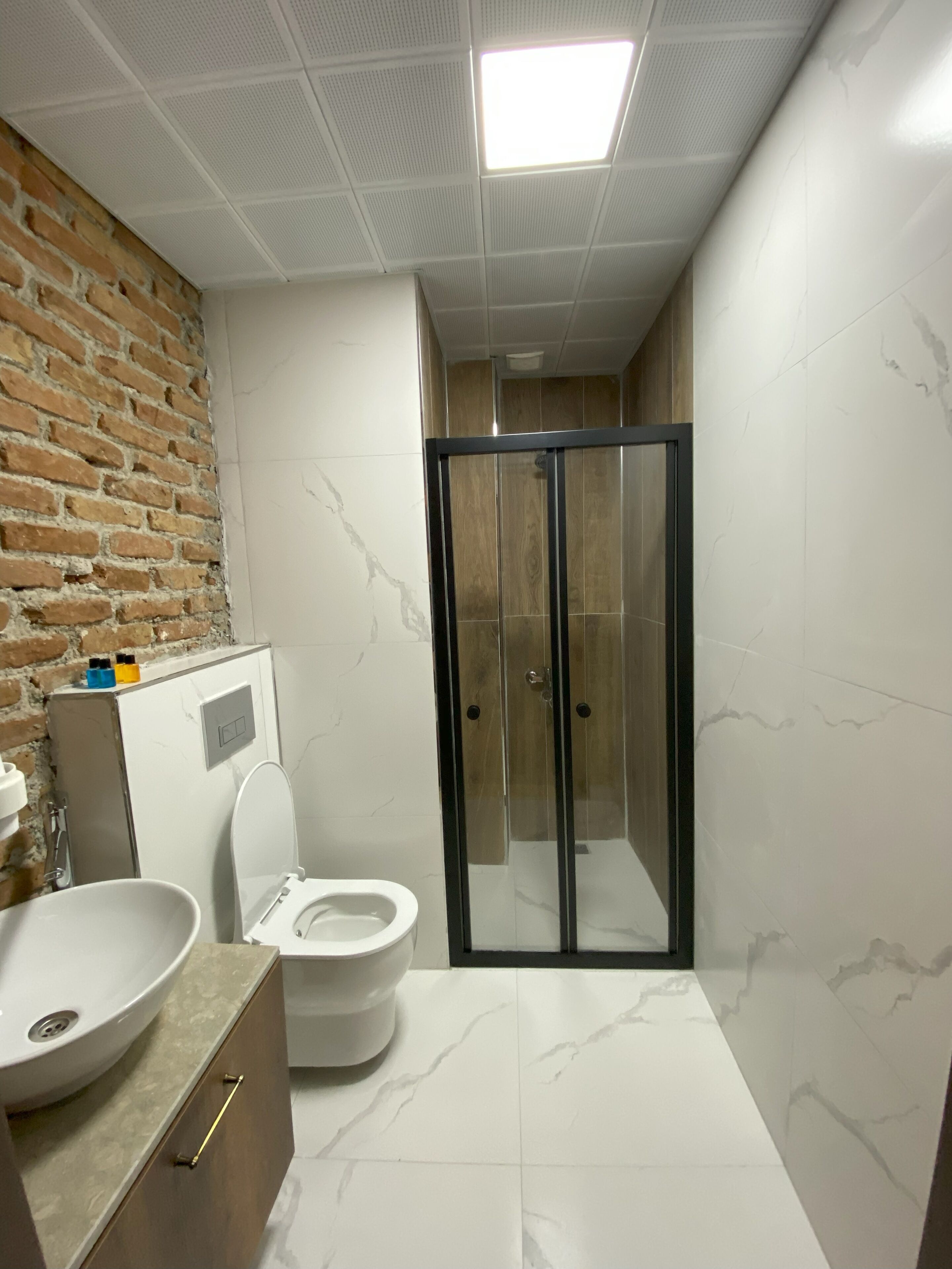 A modern bathroom with a white marble floor, a glass shower enclosure, a white toilet, and a sink with a marble basin.