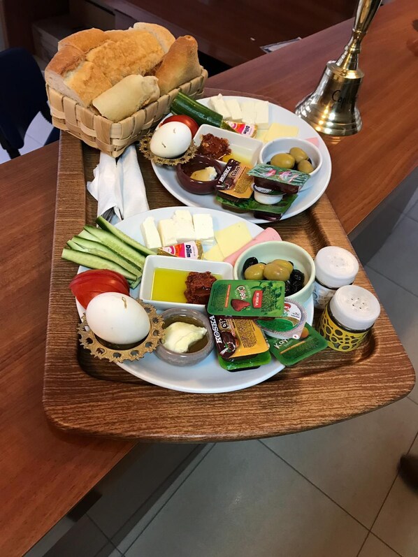 Una bandeja de madera con diversos alimentos, como pan, huevos, queso, aceitunas y salsas.