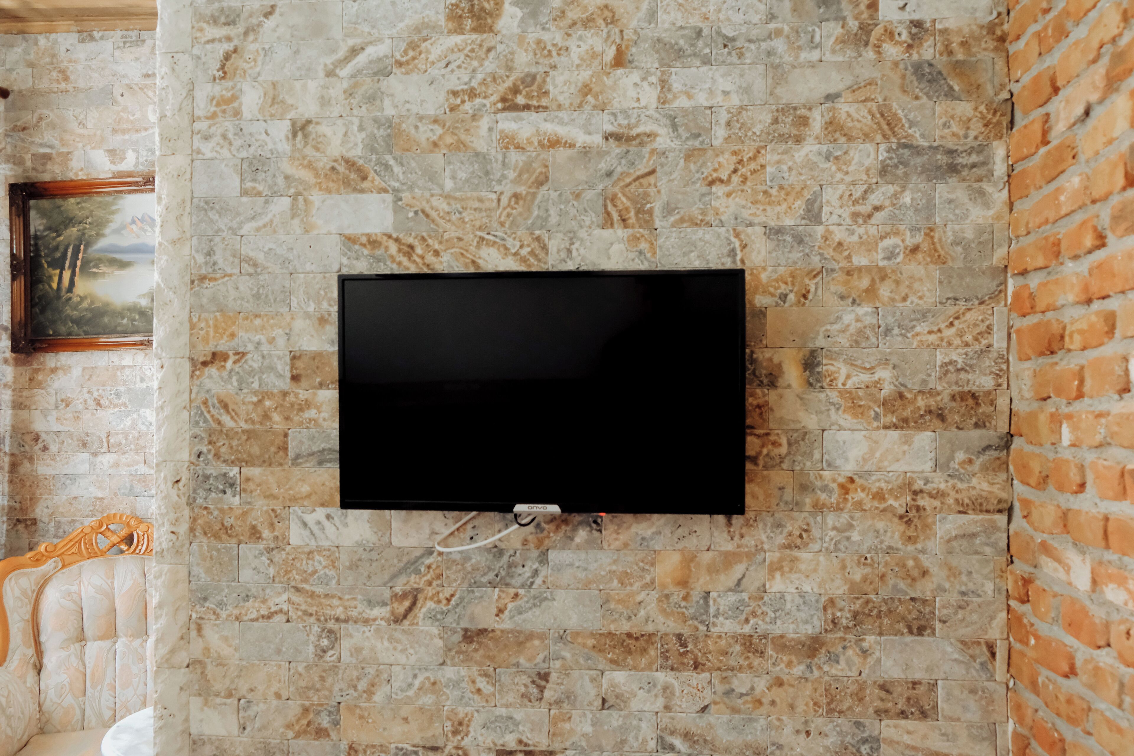 A flat-screen TV mounted on a stone wall with a picture frame to the left.