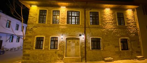 Ein zweistöckiges Steinhaus mit zahlreichen Fenstern, einem zentralen Eingang und einer kleinen Veranda.