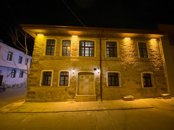 A two-story stone building with multiple windows, a central entrance, and a small porch area.