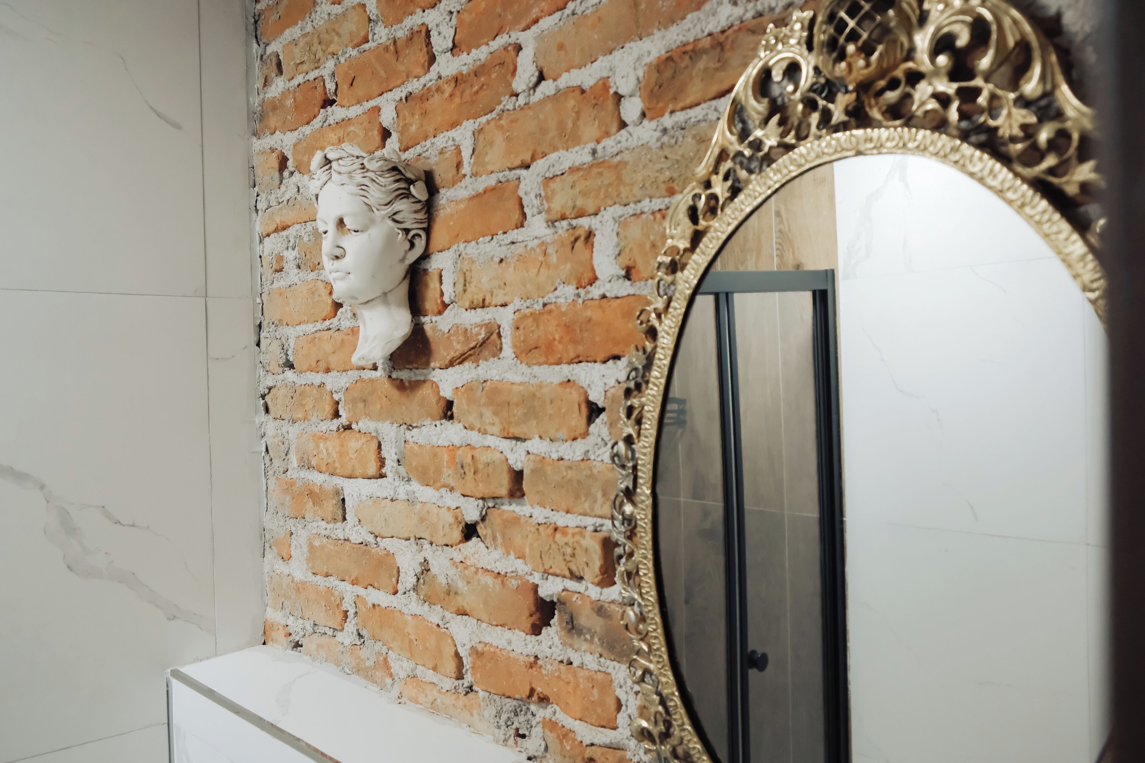 A bathroom with a brick wall, a white marble sink, and a large ornate mirror.