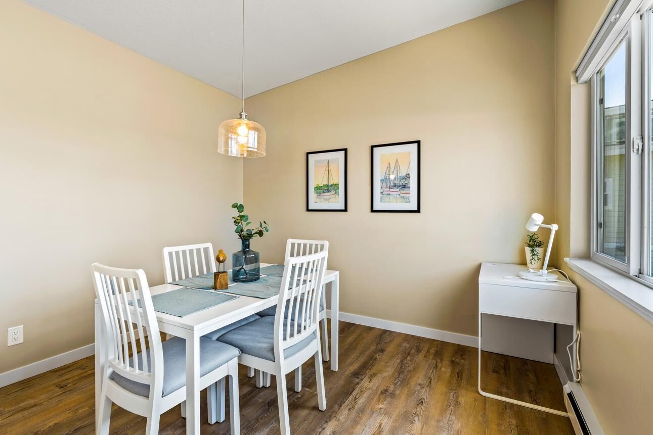 A dining area with a white table and chairs, a hanging light fixture, and framed pictures on the wall.