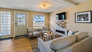 Un salon avec un canapé, des fauteuils, une cheminée et un téléviseur fixé au mur.