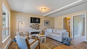 Un salon avec une cheminée, un canapé, un fauteuil, une table basse et un téléviseur fixé au mur.