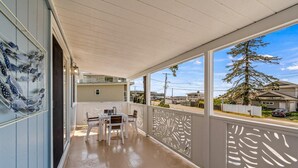 Un porche cubierto con una mesa y sillas, un muro decorativo y vistas a un árbol y casas del vecindario.