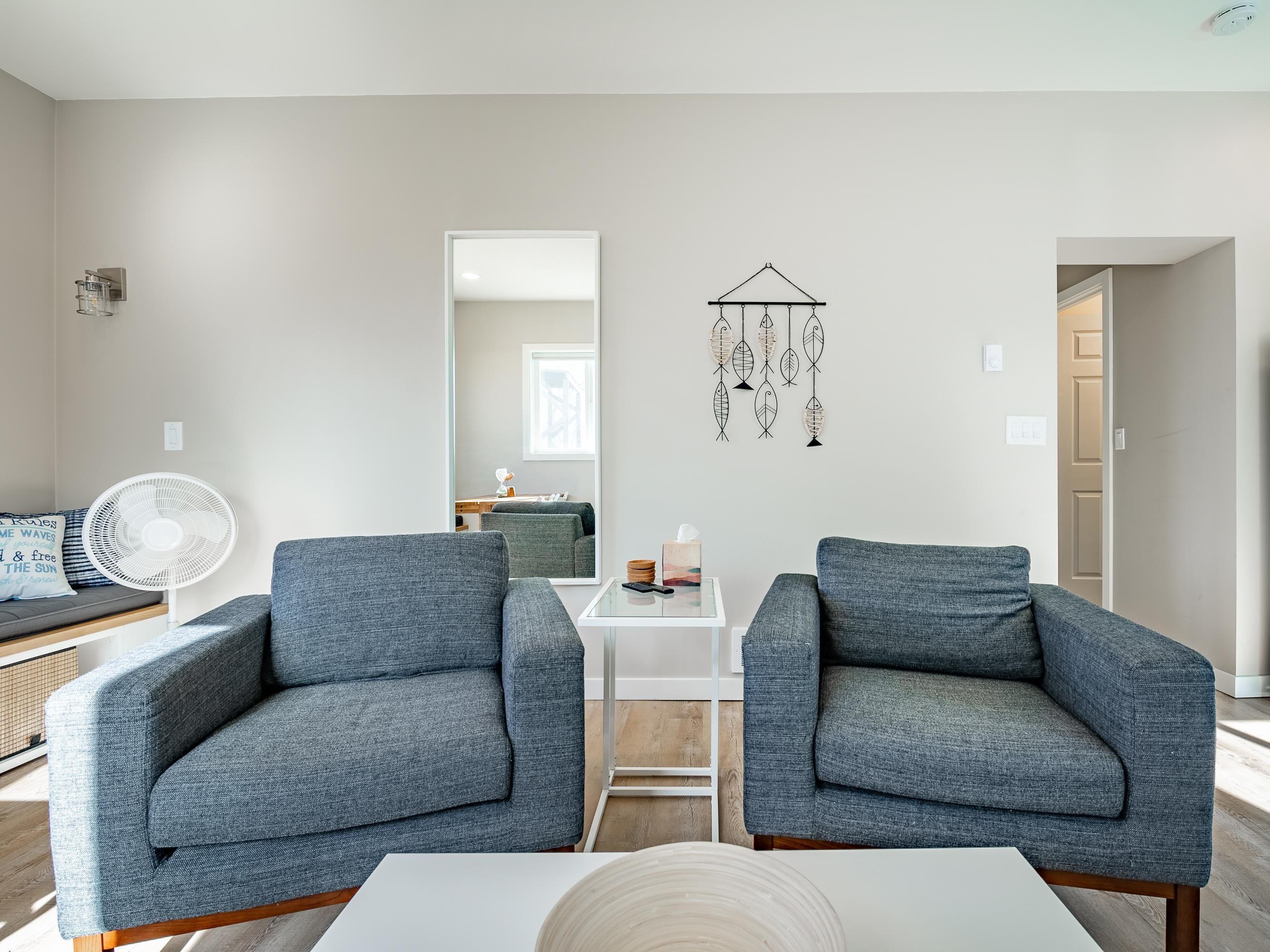 A modern living room with two grey armchairs, a white coffee table, and a wall-mounted dreamcatcher.