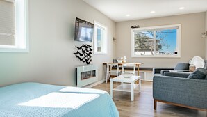 A modern living room with a large bed, a seating area with a sofa and chairs, a small table, and a fireplace.