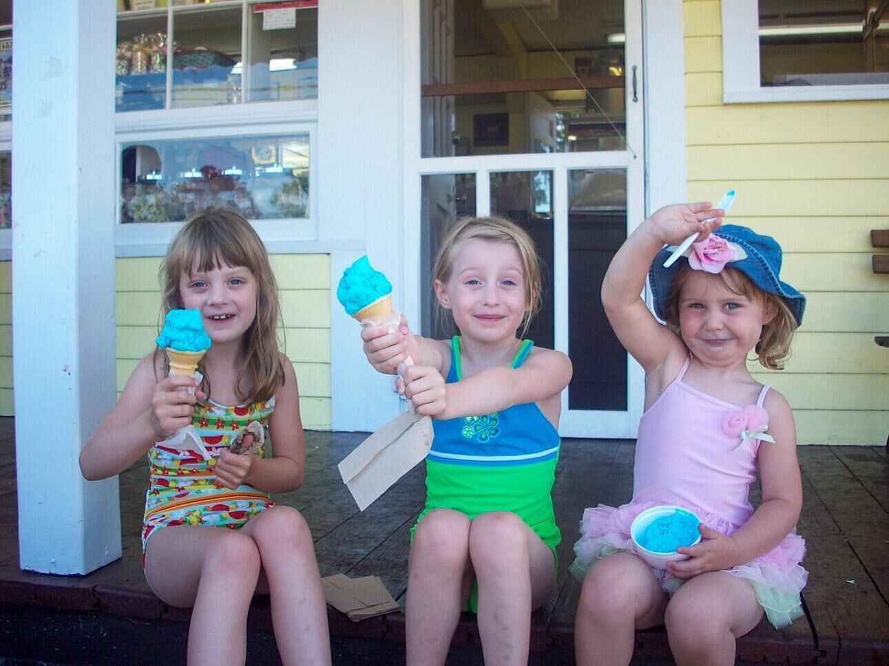 Trois enfants sont assis sur un porche, chacun tenant un cornet de glace.