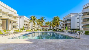 A swimming pool area with lounge chairs and palm trees, surrounded by multi-story buildings. - Steps from a beautiful beach – Your Puerto Rican Getaway Awaits (Río Grande)