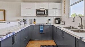 A modern kitchen with grey cabinets, a white countertop, a built-in microwave, a coffee maker, and a sink. - Steps from a beautiful beach – Your Puerto Rican Getaway Awaits (Río Grande)