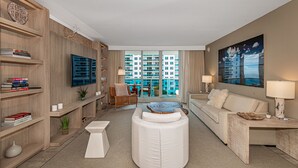 A modern living room with a sofa, ottoman, and a flat-screen TV. There are bookshelves and a dining area visible. - 1 Hotel Modern King Suite 1BR 1 5BA w Ocean View (Miami Beach)