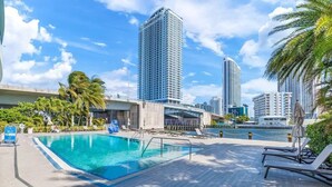 A swimming pool with lounge chairs and palm trees, surrounded by high-rise buildings. - Luxury Waterfront Condo (Hallandale Beach)