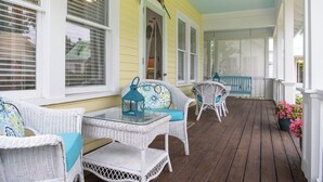 A covered porch with wicker furniture and a glass table, featuring a decorative bird and a lattice screen. - THE FAMILY REUNION COMPOUND AT OLD COLORADO INN (Stuart)