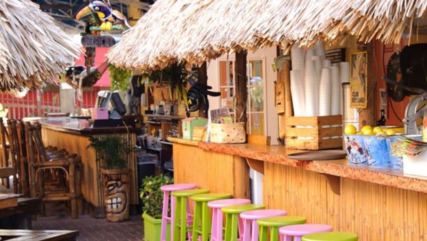 A tiki bar with a thatched roof, wooden counter, and colorful stools. - THE FAMILY REUNION COMPOUND AT OLD COLORADO INN (Stuart)