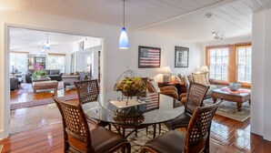 A spacious living room with a round glass coffee table surrounded by wooden chairs, a glass-top dining table, and a large window with blinds. - THE FAMILY REUNION COMPOUND AT OLD COLORADO INN (Stuart)