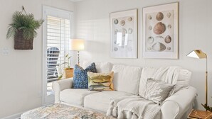 A living room with a white couch, a patterned rug, a wall-mounted plant, and framed artwork.