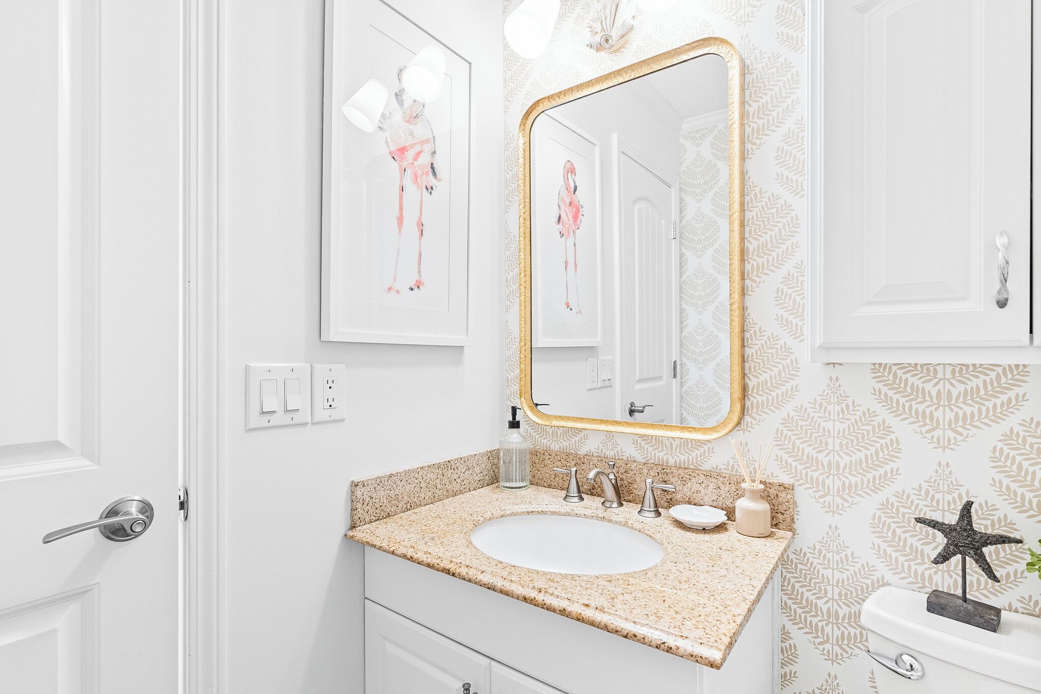 Een badkamer met een witte wastafel, een spiegel met gouden lijst en behang met een patroon.