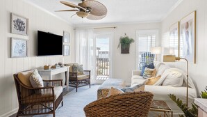 A living room with a ceiling fan, a flat-screen TV, wicker furniture, a white sofa, and a balcony with a view.